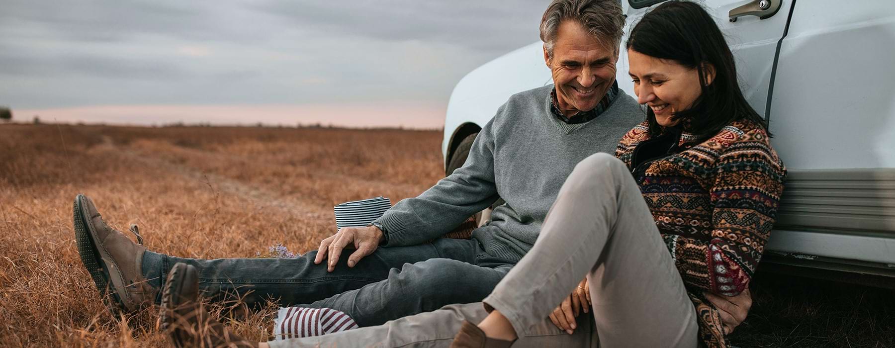 couple relaxing against car in field